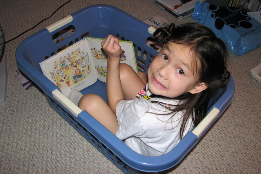 Cookies & Clogs | Everything changes when you have kids. Parenthood makes you do and say things you never thought you'd do when raising children. See how our parenting experience has gone and what two things have helped with cleaning up their messes. Child in laundry basket reading with mischievous expression.
